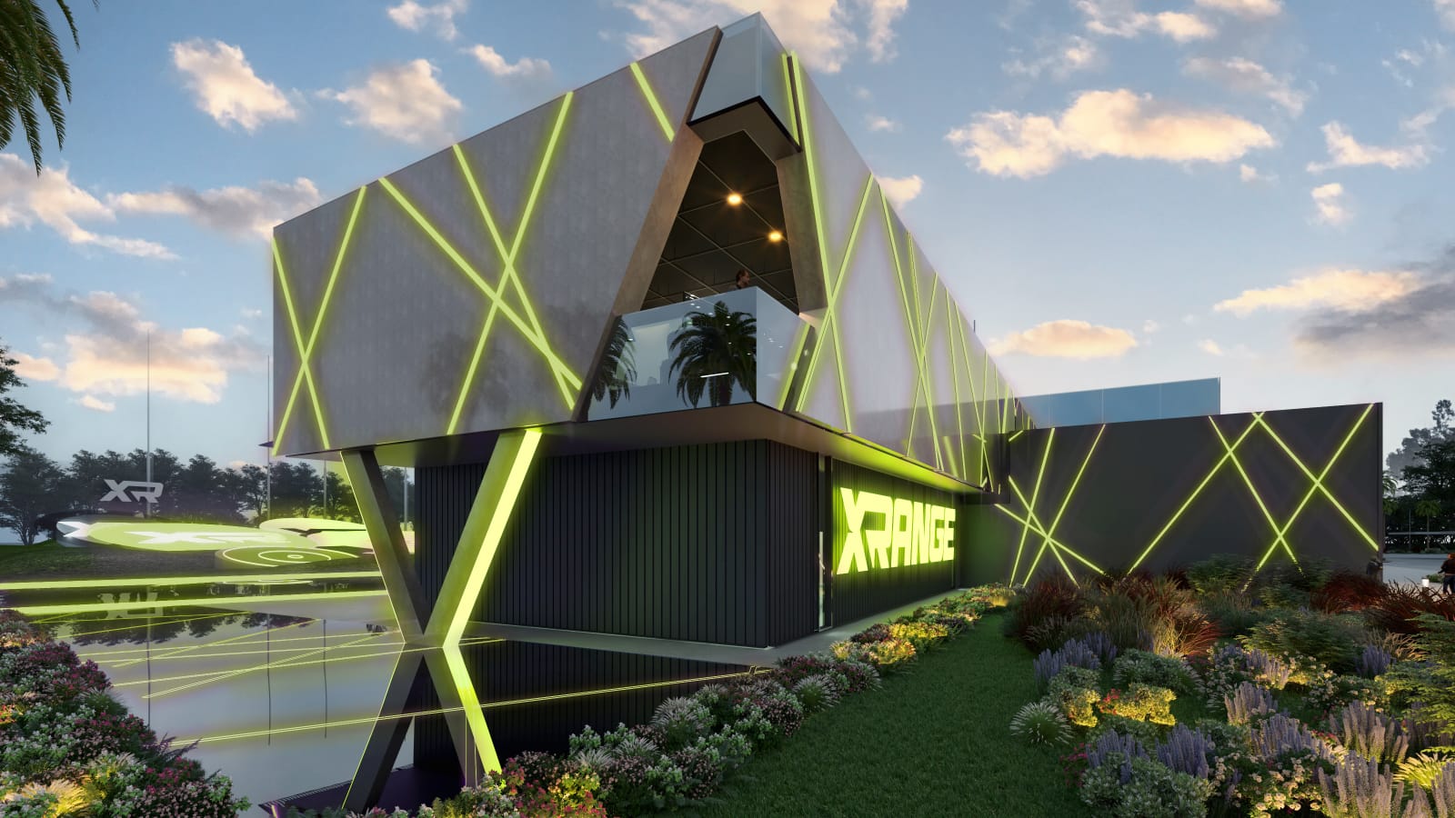 Angled view of the XRANGE clubhouse beside a reflecting pool, with the cantilevered upper floor and green structural lighting mirrored in the water.